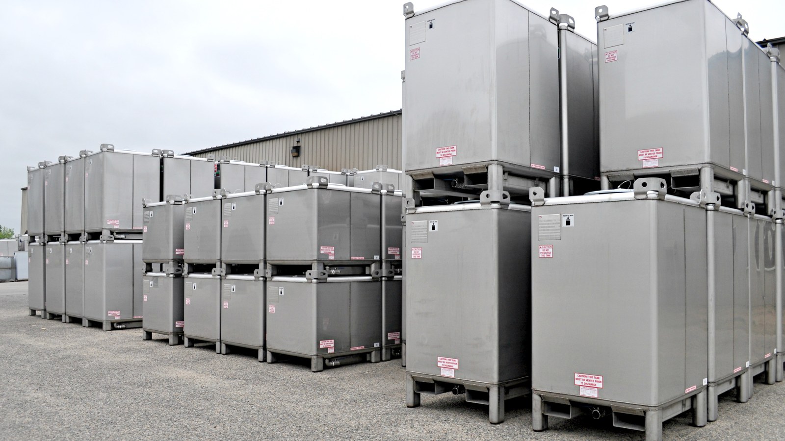 Rows of square stainless steel IBC totes stacked two high in an outdoor storage yard