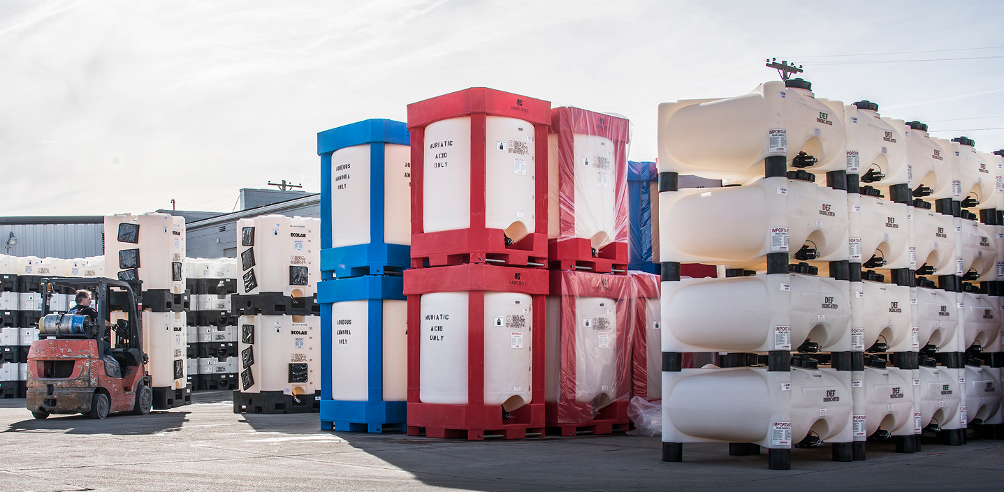 Rows of stacked IBC totes and caged bulk containers in an outdoor Canadian distribution yard