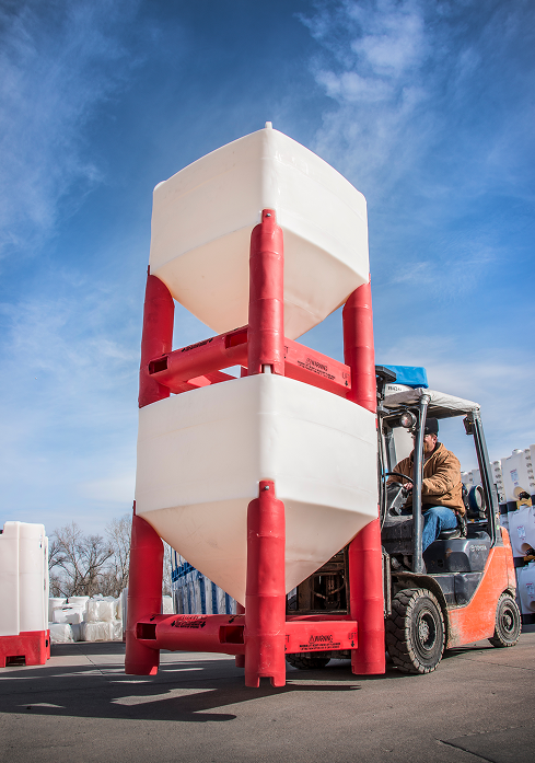 Forklift lifting two stacked white and red cone-bottom bulk containers in a Durastar yard